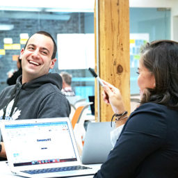 Two colleagues smiling and discussing work at a table.