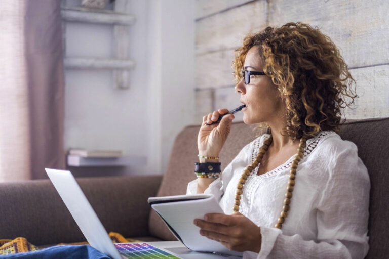 A woman brainstorming ideas for leading innovation, working on a laptop with a notepad in hand.