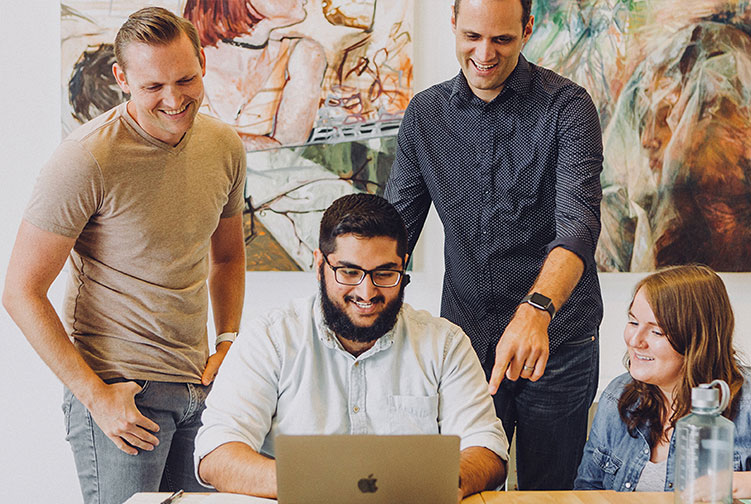 A diverse team of professionals smiling while collaborating on a laptop, illustrating business impact and teamwork.