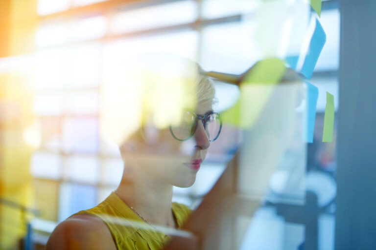 A woman is brainstorming ideas on a glass wall with sticky notes.