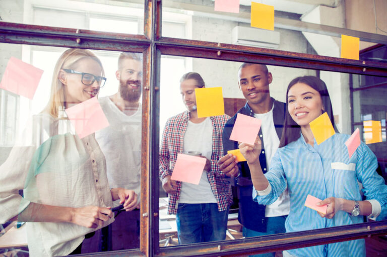 A diverse team collaborating with sticky notes on a glass wall during an ExperienceInnovation™ | Learn session.