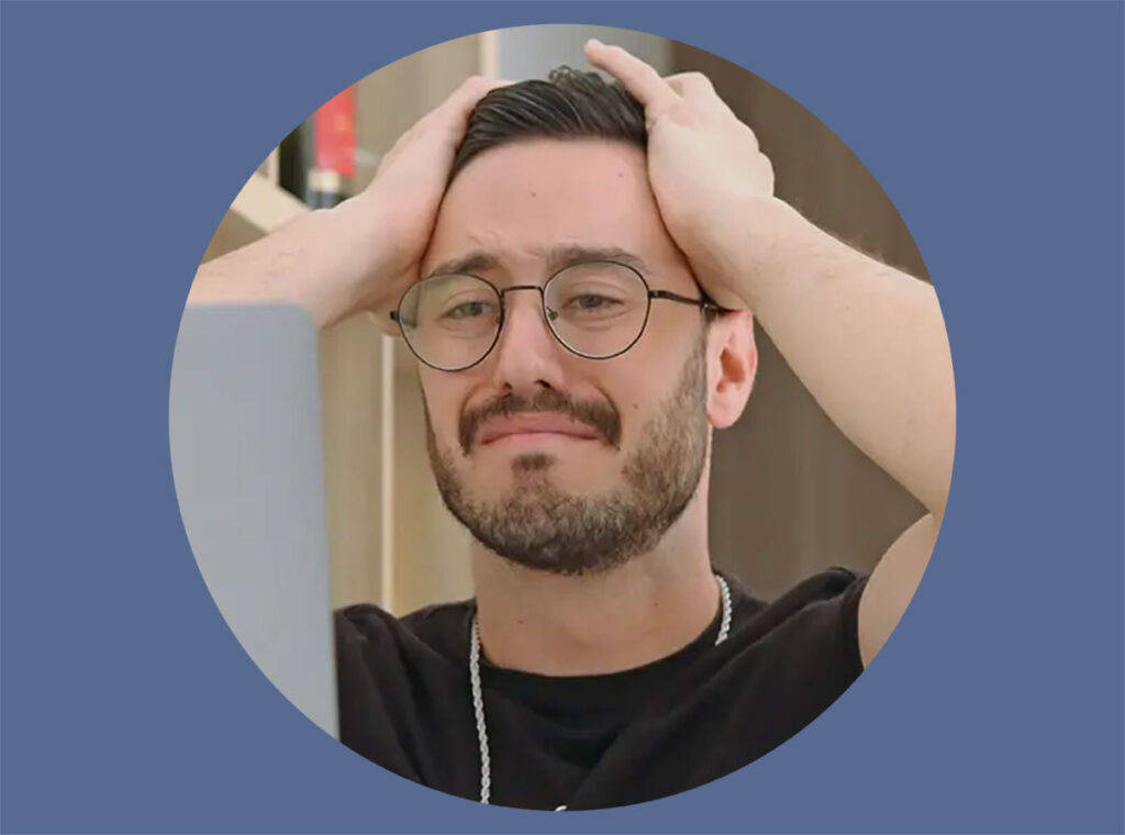 A man working on his laptop with a frustrated expression and his hands on his head.